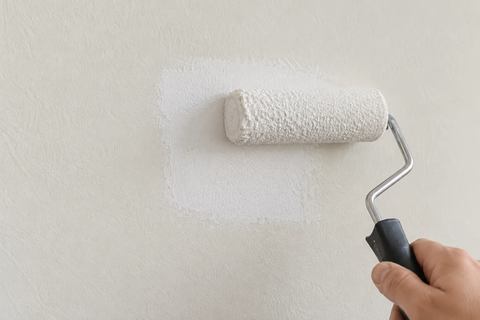 Small paint roller applying a thin white primer coat over a smooth wall repair