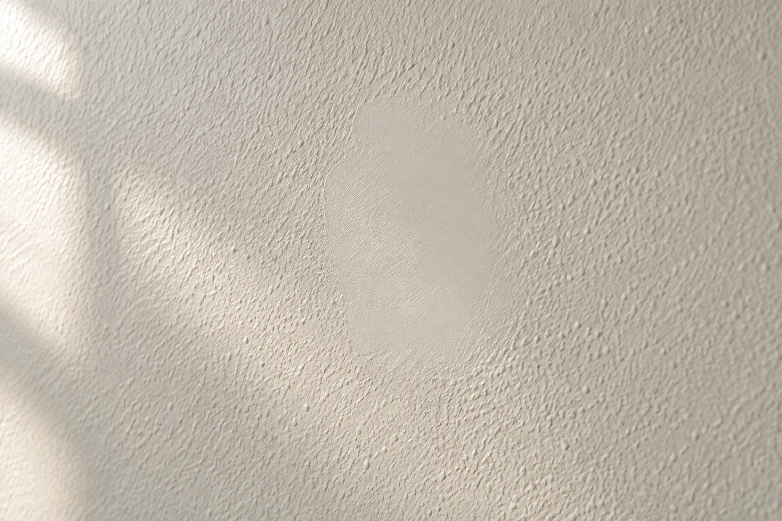 Raking light revealing a smoother repair patch within lightly textured wall paint