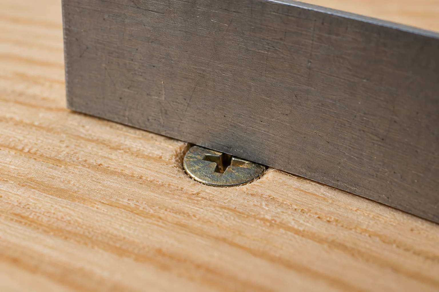 A steel straightedge crossing a countersunk screw head at the wood surface